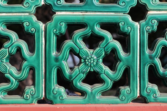 A series of decorative green ceramic tiles with intricate floral patterns and swirls, bordered with a red base. The tiles form a symmetrical design and have a glossy finish.