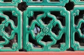 A series of decorative green ceramic tiles with intricate floral patterns and swirls, bordered with a red base. The tiles form a symmetrical design and have a glossy finish.