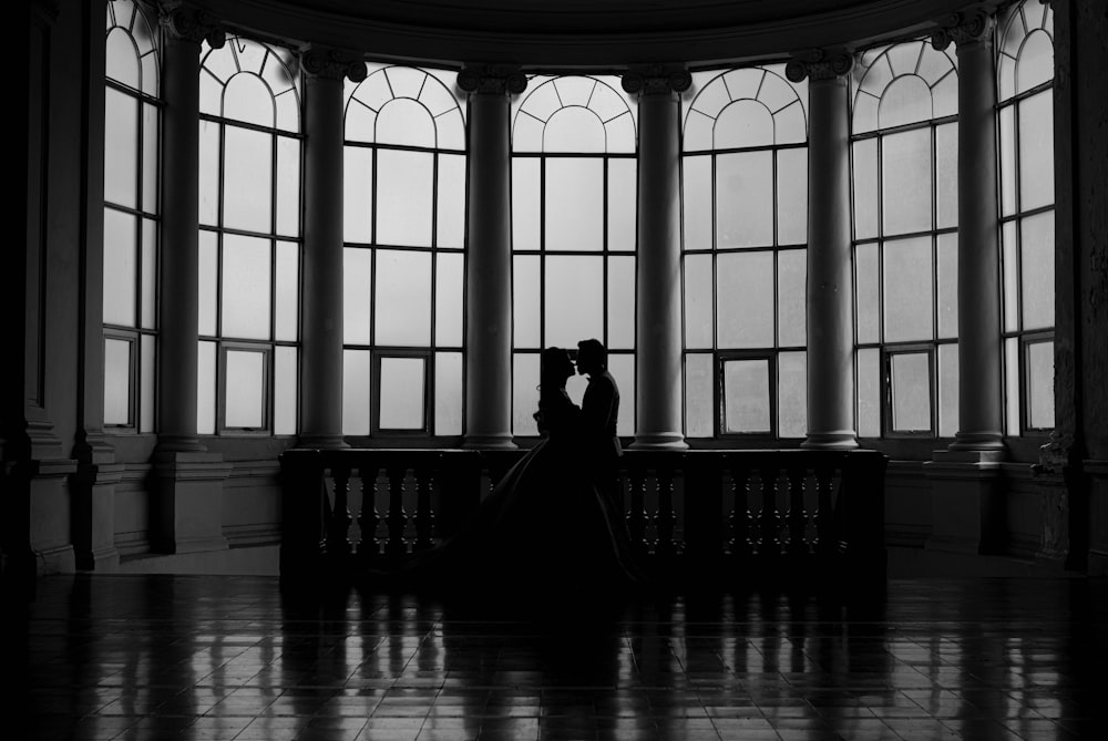 a bride and groom standing in front of large windows