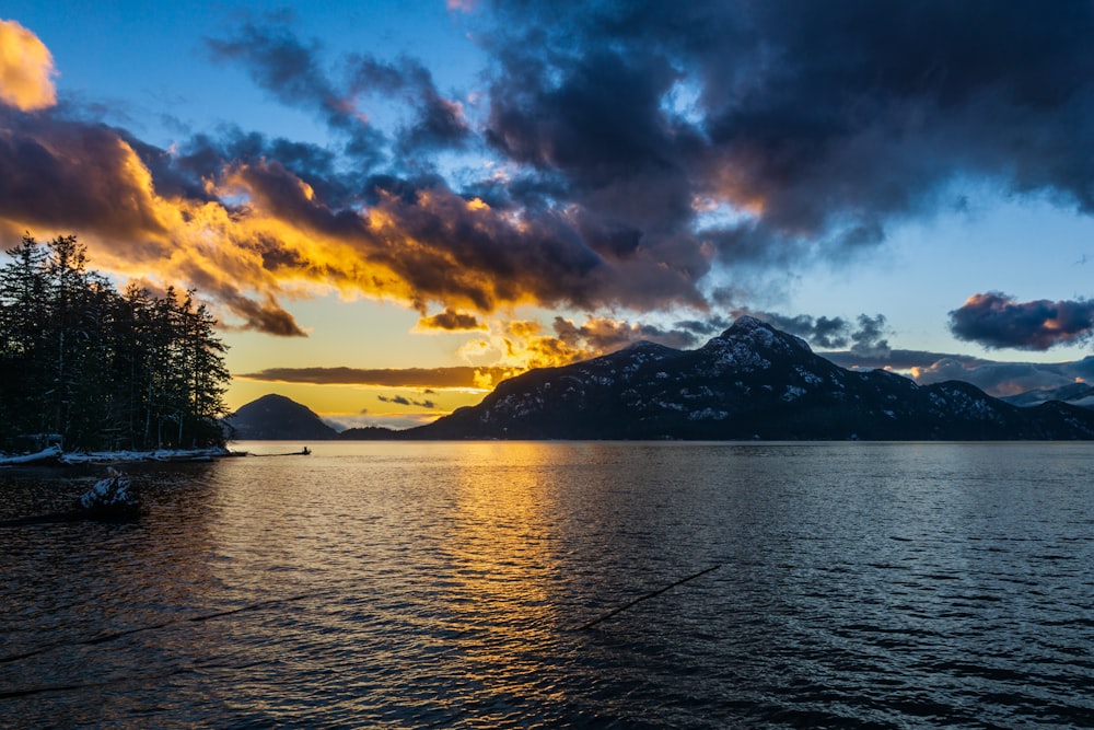 the sun is setting over a lake with mountains in the background