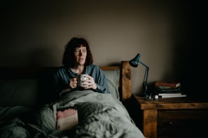a woman sitting on a bed holding a cup of coffee