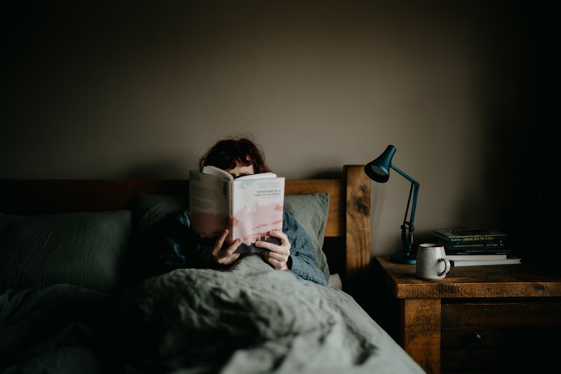 Woman reading a book in bed with cozy linens and a bedside lamp, capturing a restful pre-sleep routine for seniors