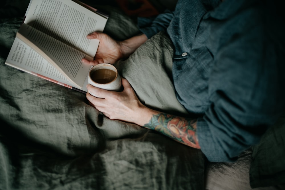 a person laying on a bed with a book and a cup of coffee