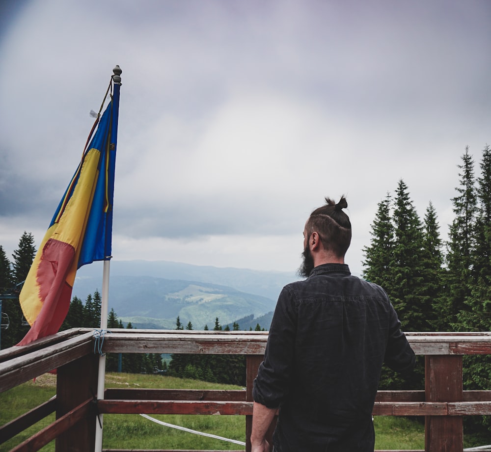 um homem em pé em cima de um deck de madeira ao lado de uma bandeira