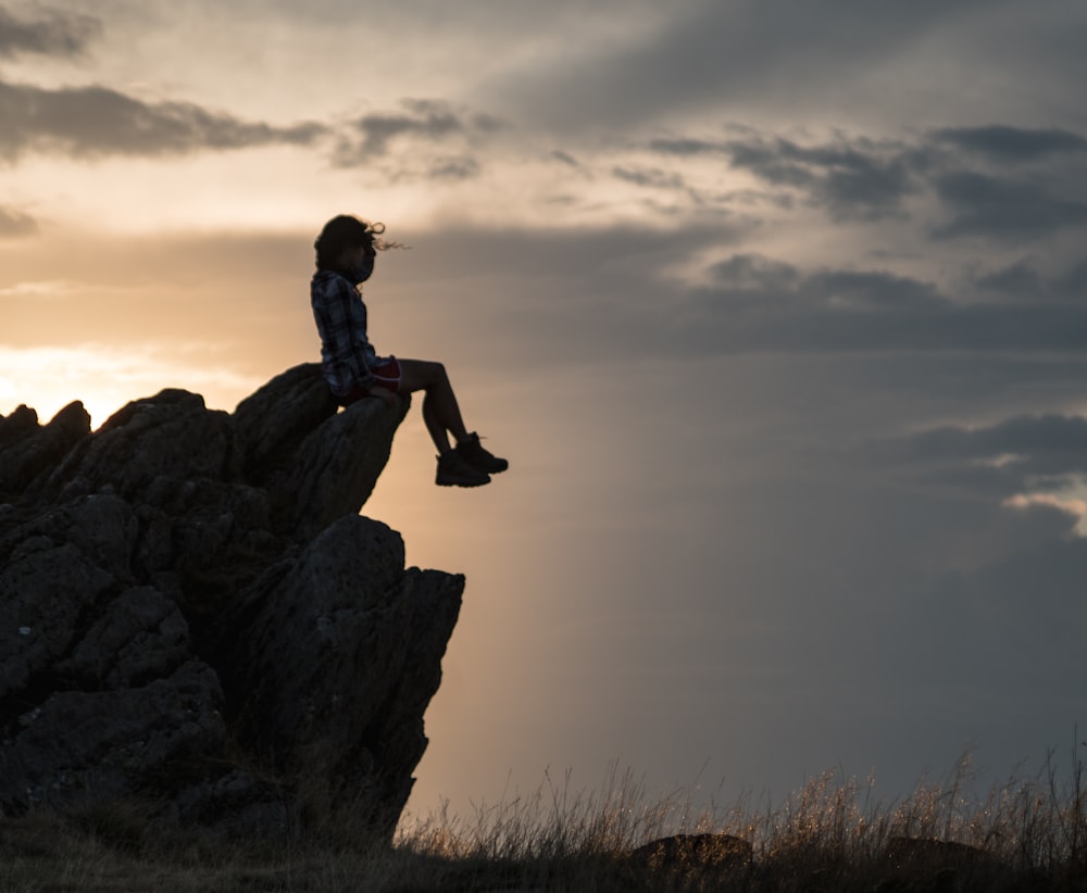 une personne assise au sommet d’un gros rocher