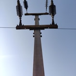 Close-up of a freshly installed high-tension concrete pole standing tall against a clear sky.