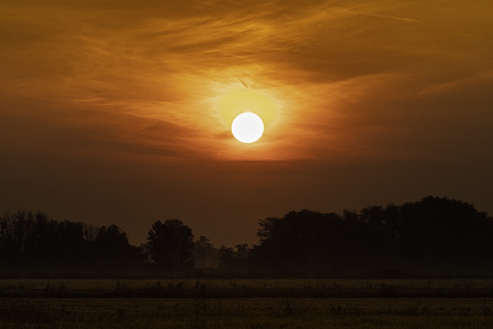 the sun is setting over a field with trees