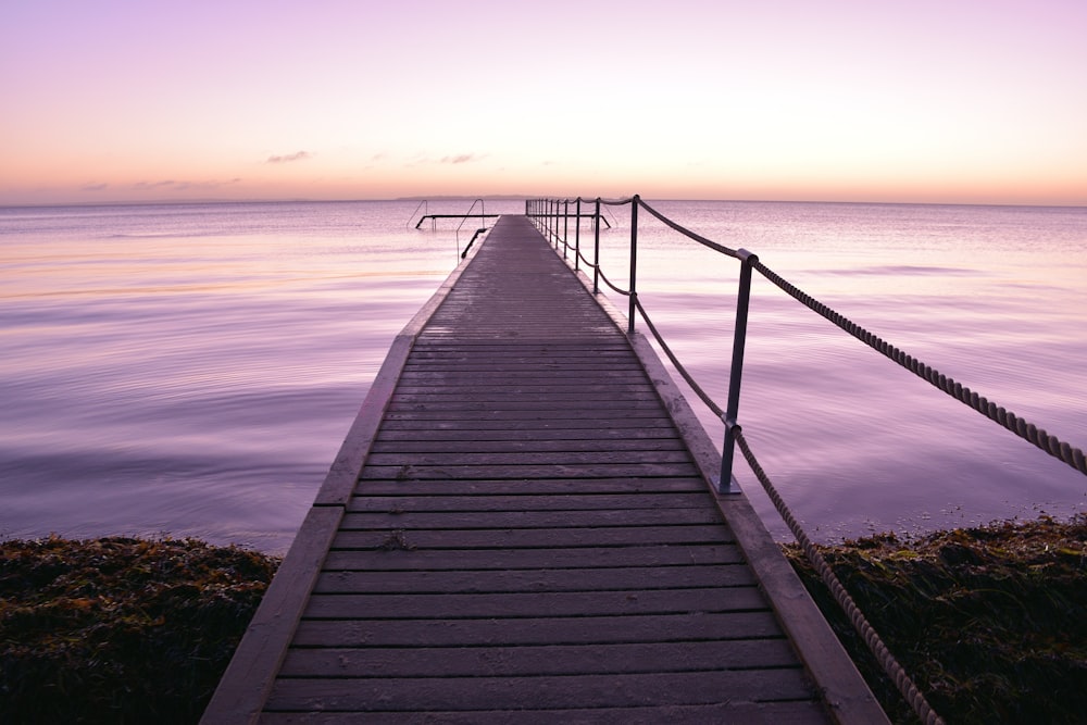a long dock leading into the ocean at sunset