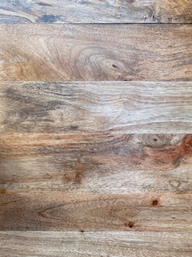 Wooden surface featuring a series of natural grain patterns and textures in various shades of brown. The planks are aligned horizontally, showcasing knots and swirling lines that add a rustic appearance.