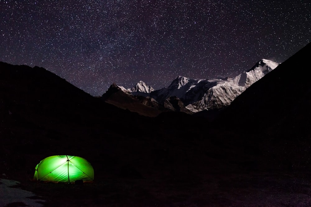 a green tent in the mountains under a night sky