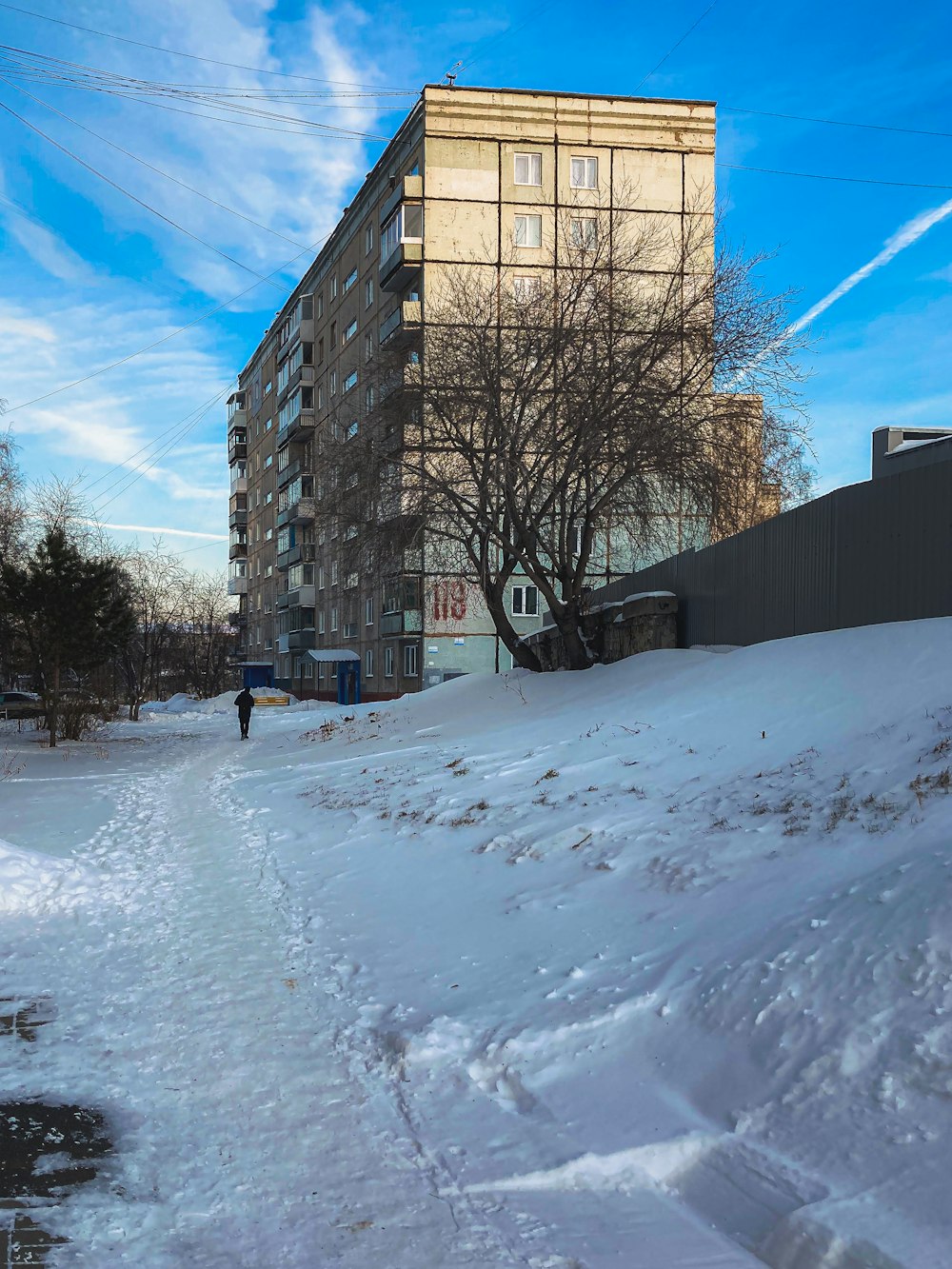 a man walking down a snow covered street next to a tall building