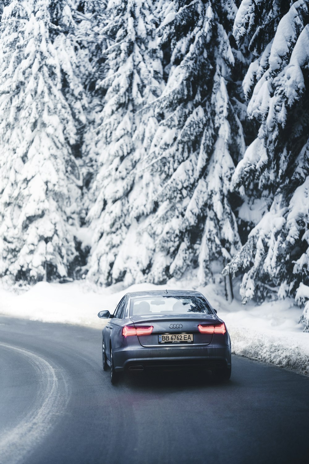 Ein Auto fährt eine verschneite Straße neben einem Wald hinunter