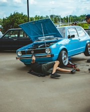 a man laying on the ground next to a blue car