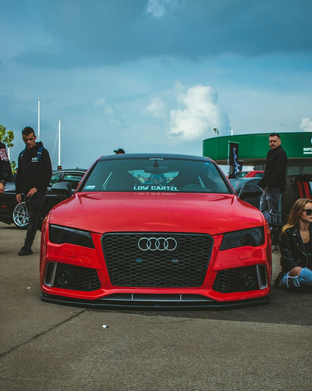 a group of people standing around a red car