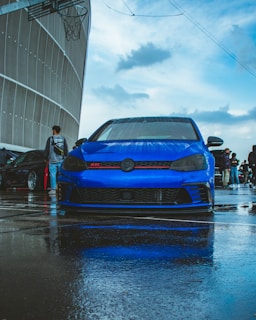 a blue car parked in a parking lot on a rainy day