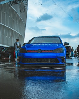 a blue car parked in a parking lot on a rainy day