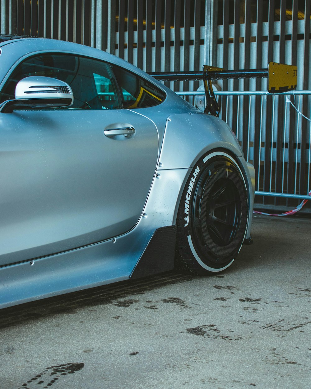 a blue sports car parked in front of a fence