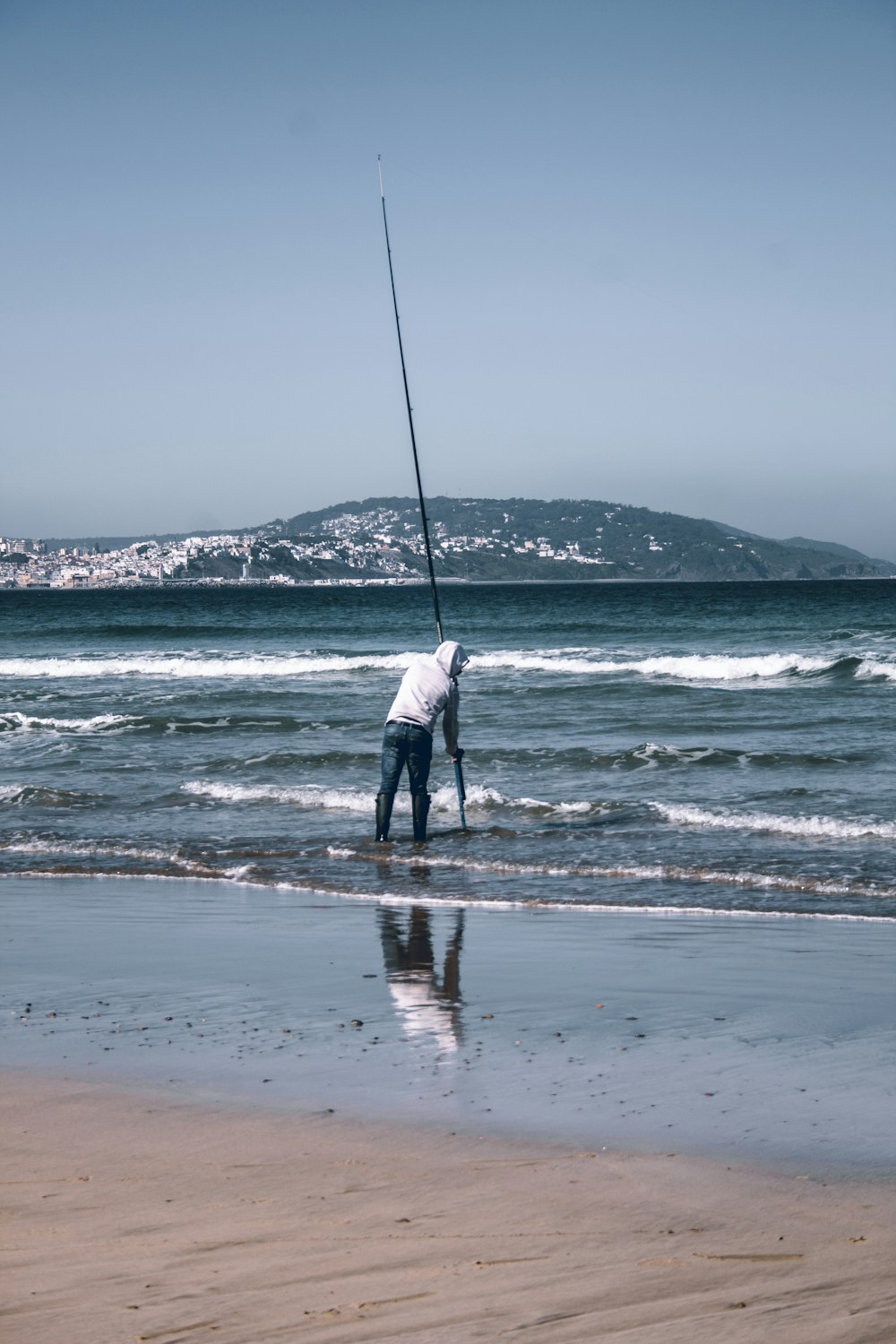 a man standing on top of a beach holding a fishing pole