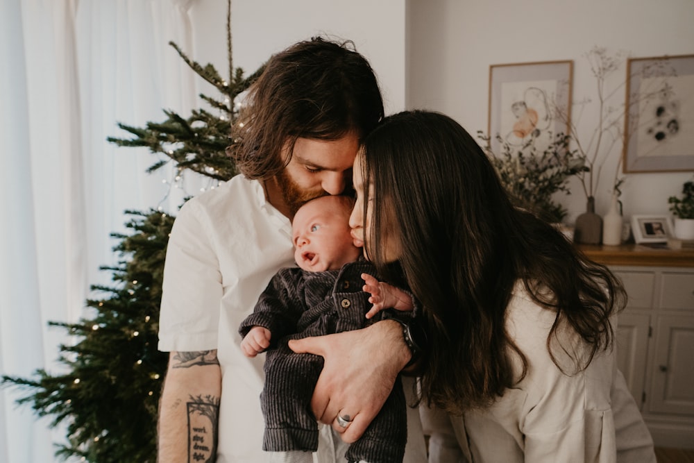 a man and woman holding a baby near a christmas tree