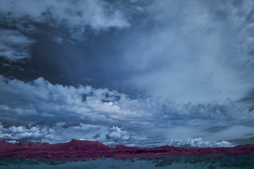 a cloudy sky over a desert landscape with mountains in the distance