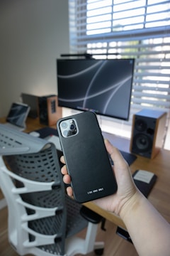 Close-up of hands inspecting a smartphone in a bright workspace.