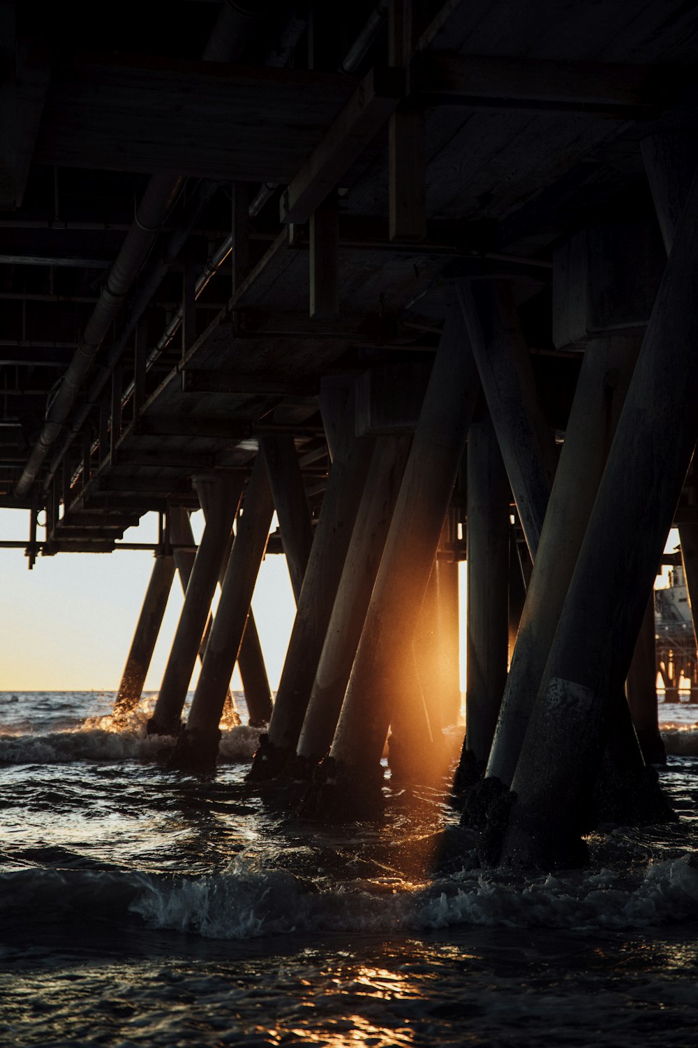 the sun shines through the water underneath a pier