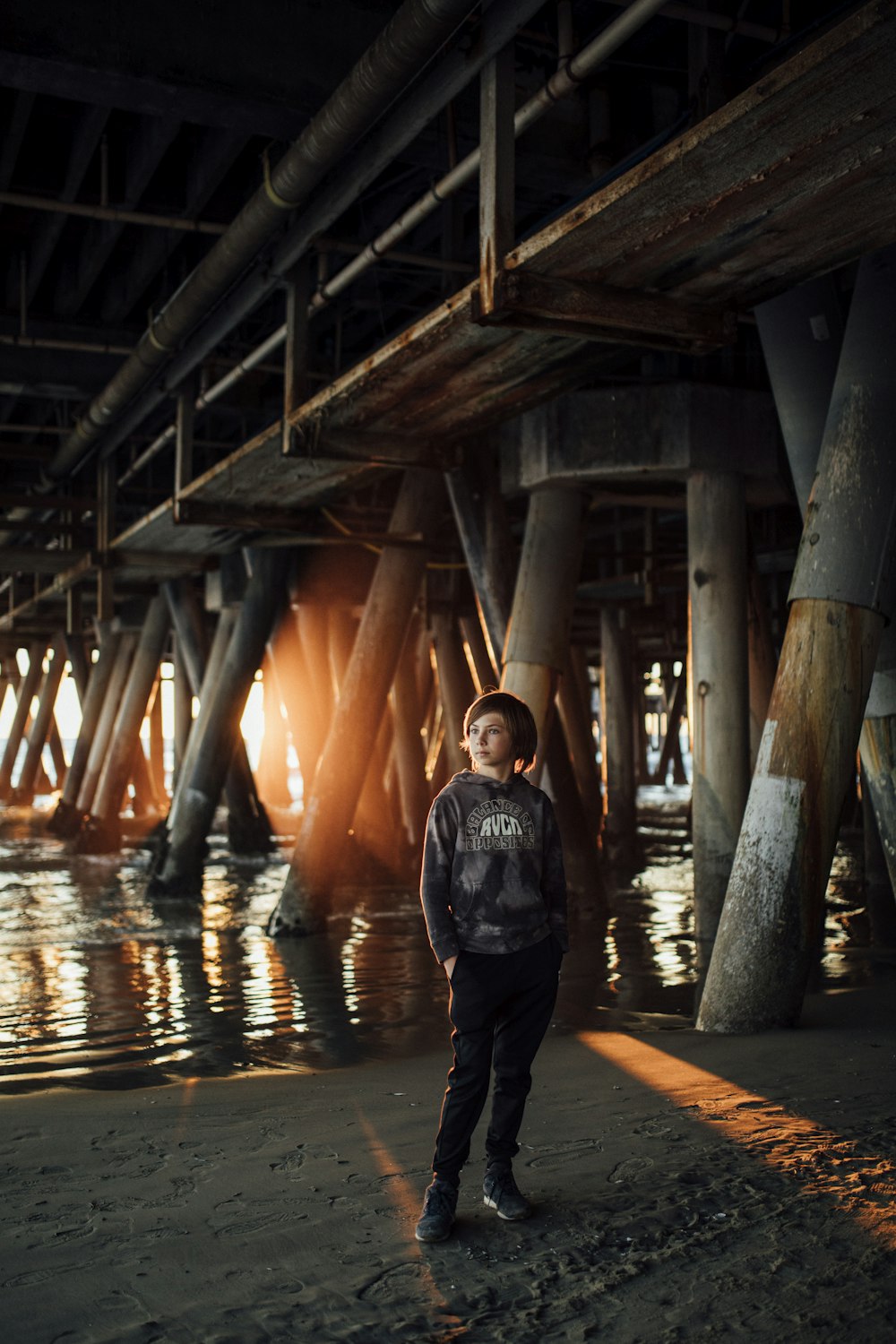 a young boy standing under a bridge next to a body of water