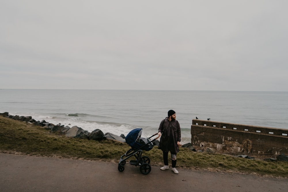 a man standing next to a baby stroller near the ocean