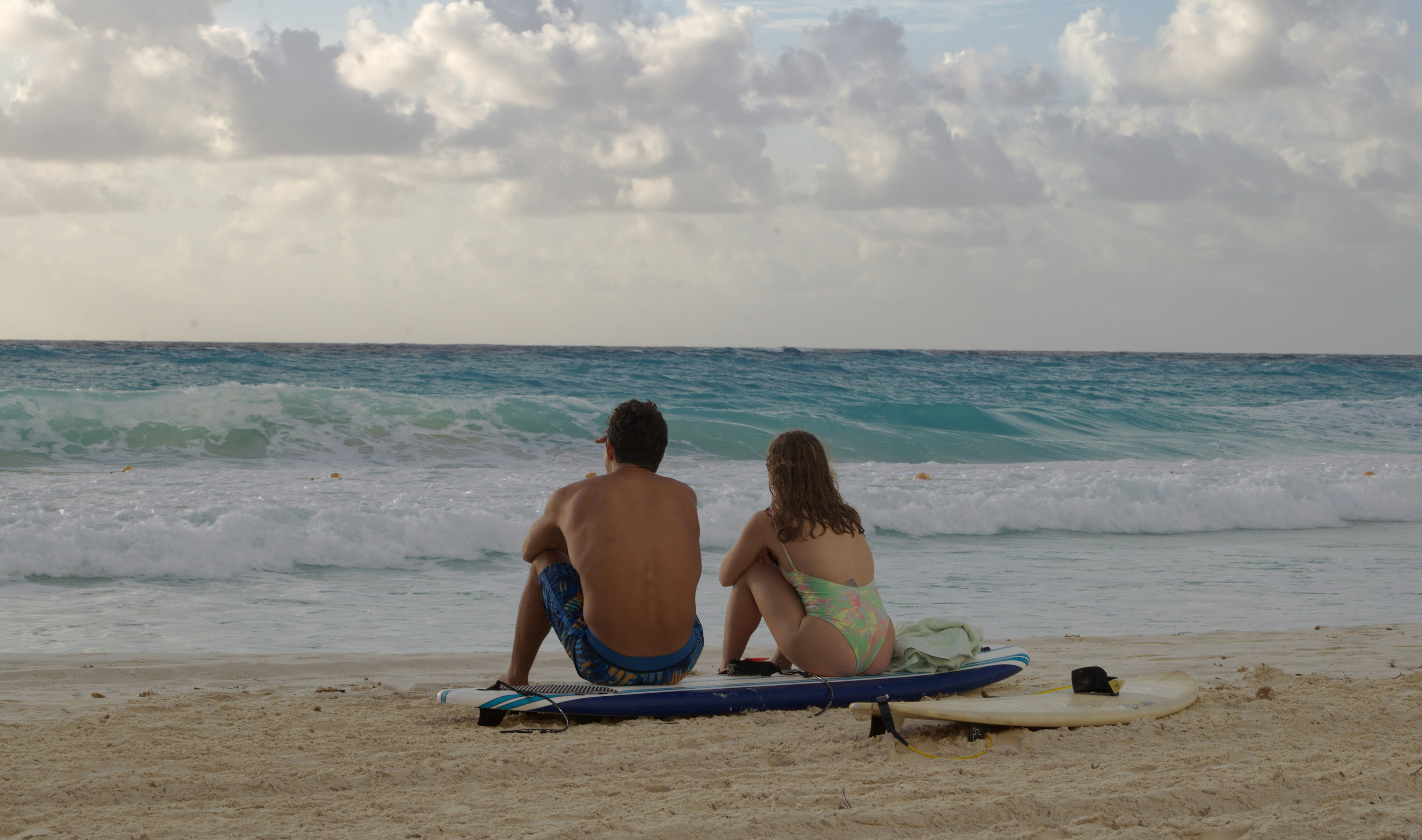 a man and a woman sitting on a surfboard on the beach
