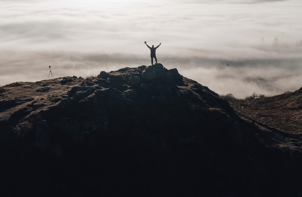 une personne debout au sommet d’une montagne, les bras en l’air