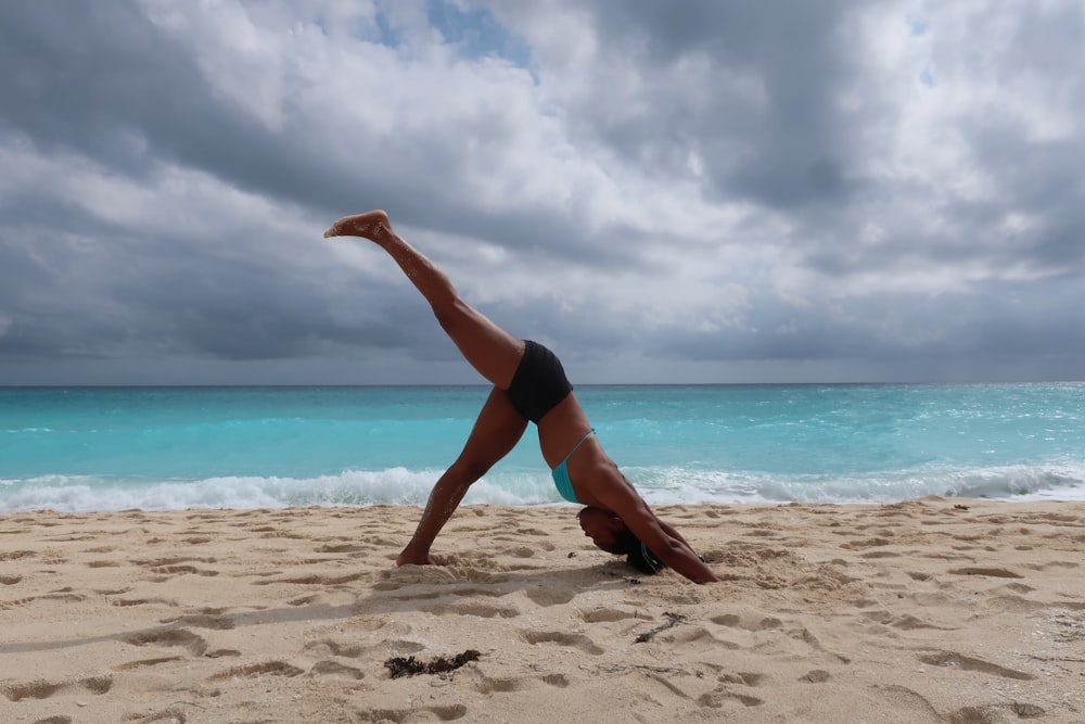 a woman doing a handstand on the beach