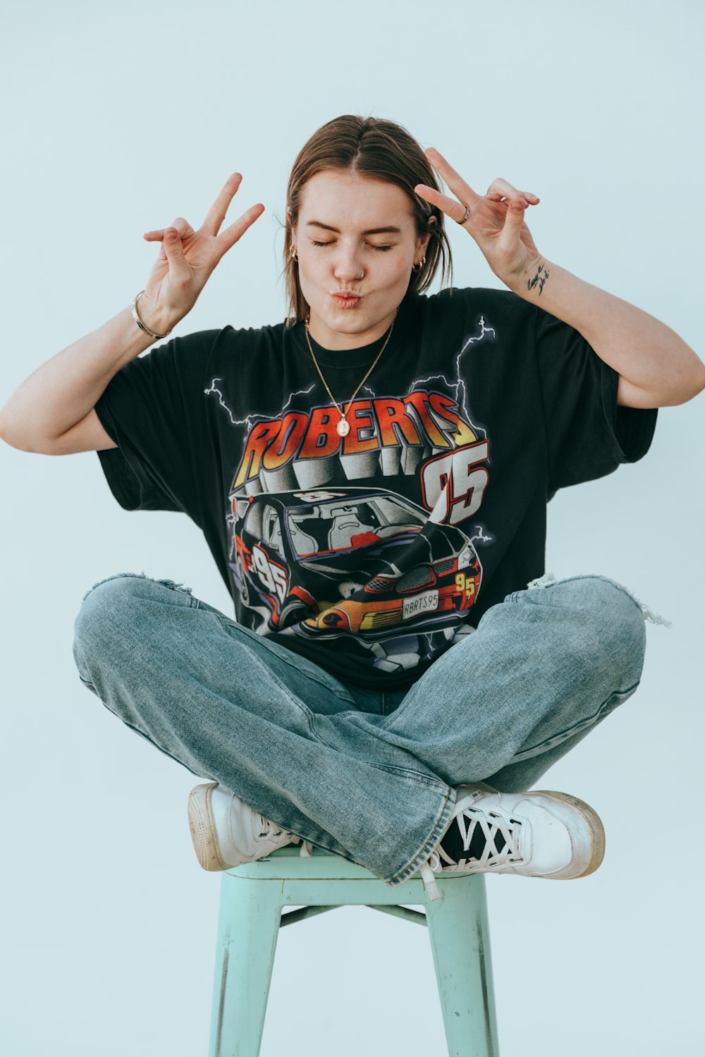 a woman sitting on a stool with her hands in the air