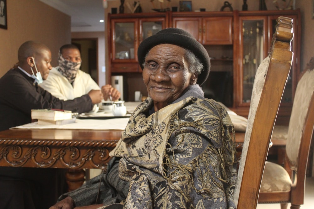 an old woman sitting at a table with two men in the background