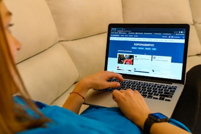 A person is sitting on a couch using a laptop, which displays a webpage in Russian related to coronavirus. The individual is casually dressed and wearing a smartwatch. The setting appears relaxed and home-like.