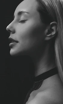 A serene portrait of Rina Kelly softly lit against a minimalist white backdrop, embodying quiet confidence.