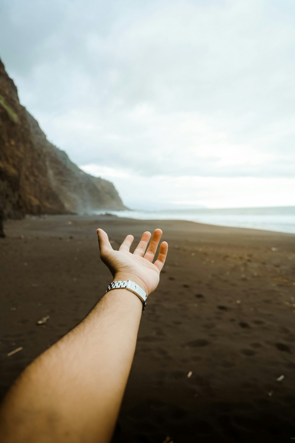 a hand reaching out towards the ocean on a cloudy day