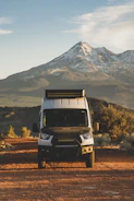 A rugged van parked beside a dirt road under a warm sunset, mountains in the background.