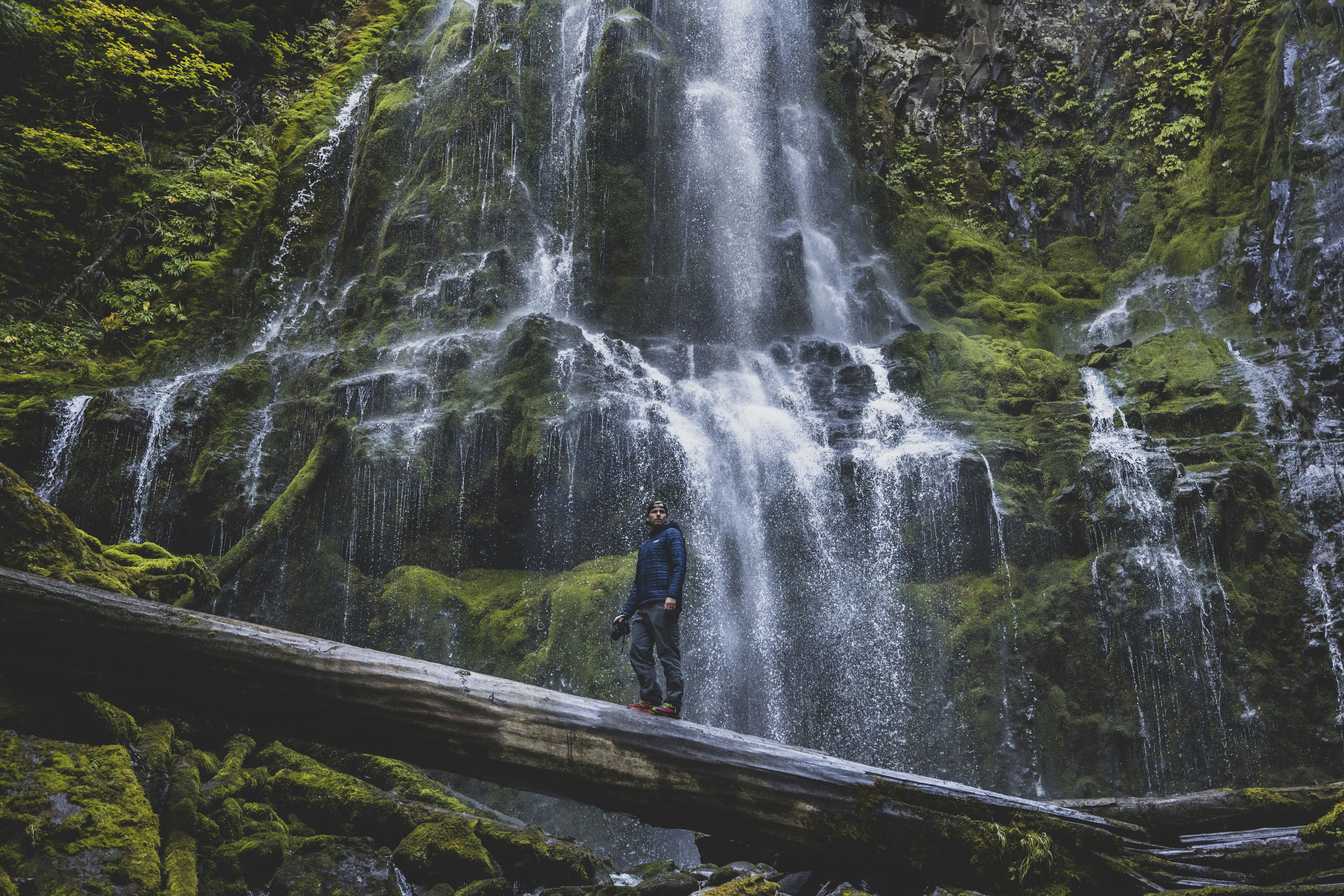 a man standing on a log in front of a waterfall