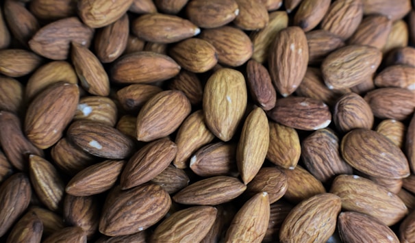 A close-up view of a pile of raw almonds, showcasing their textured brown shells with grooves and variations in tone.