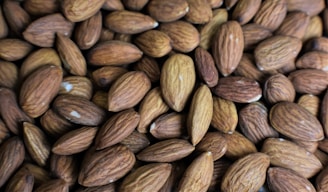 A close-up of fresh, shelled almonds spilling from a rustic burlap sack onto a cream-orange background.