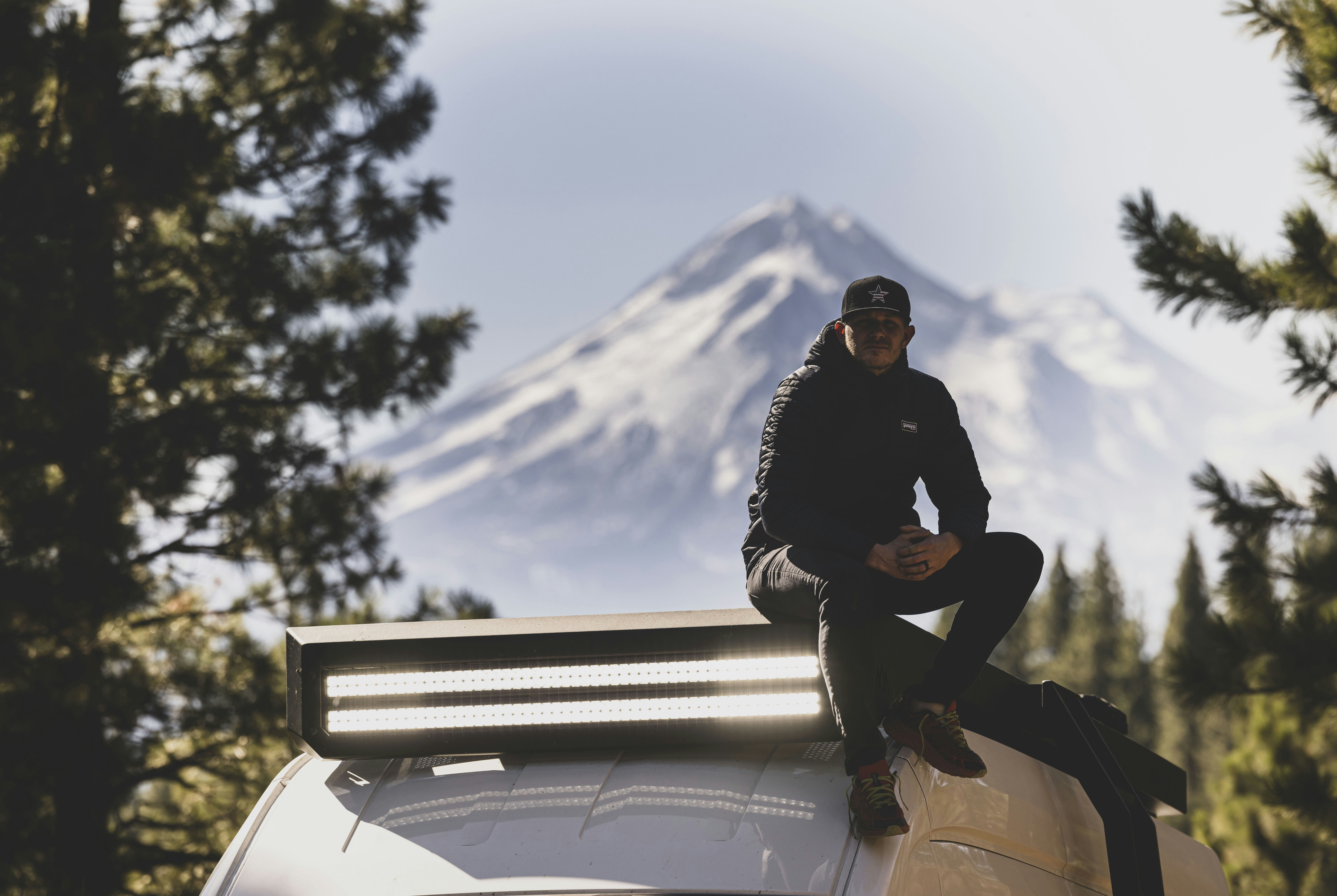 a man sitting on top of a car in front of a mountain