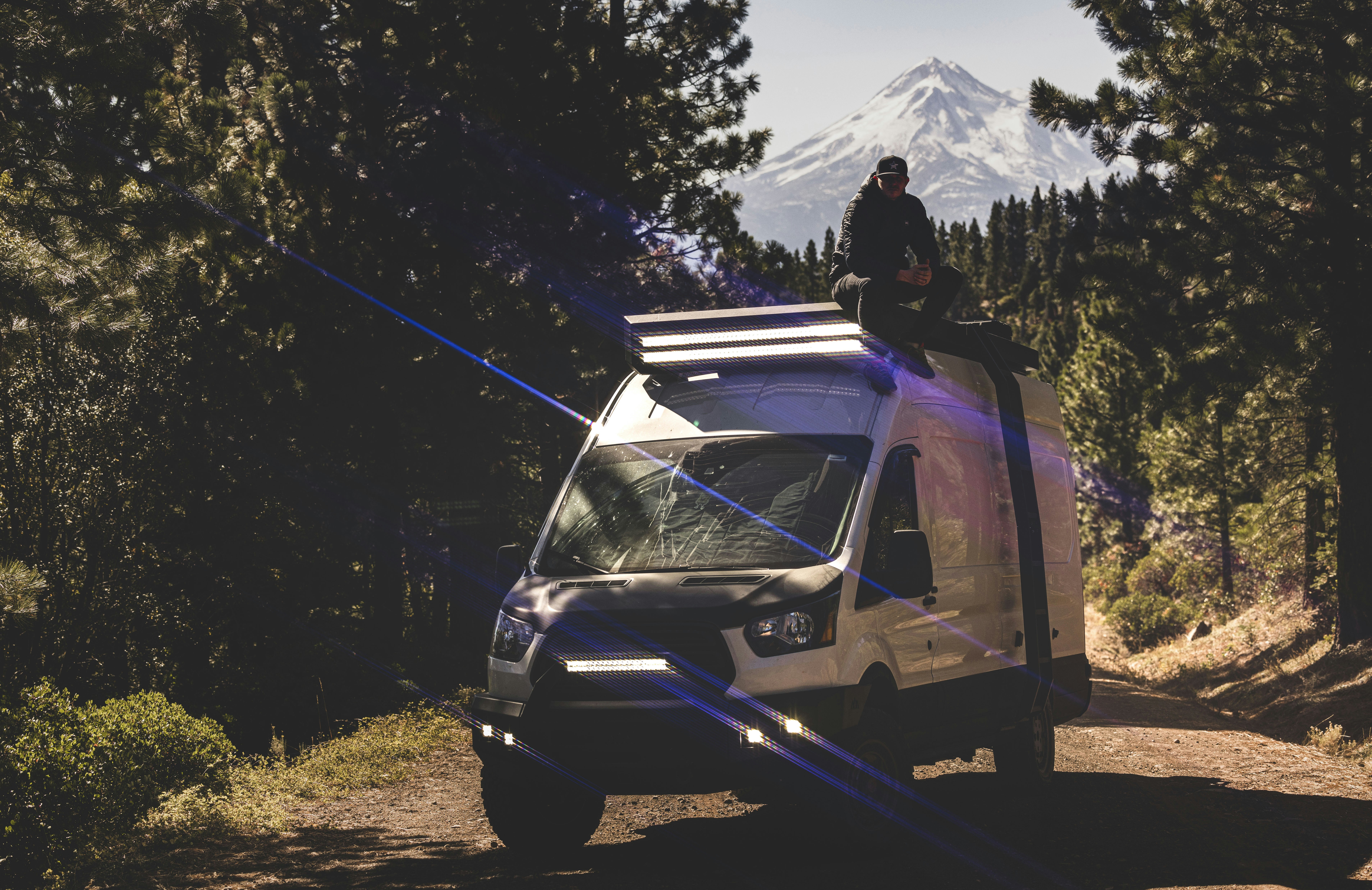 a man sitting on top of a van on a dirt road, adventure travel
