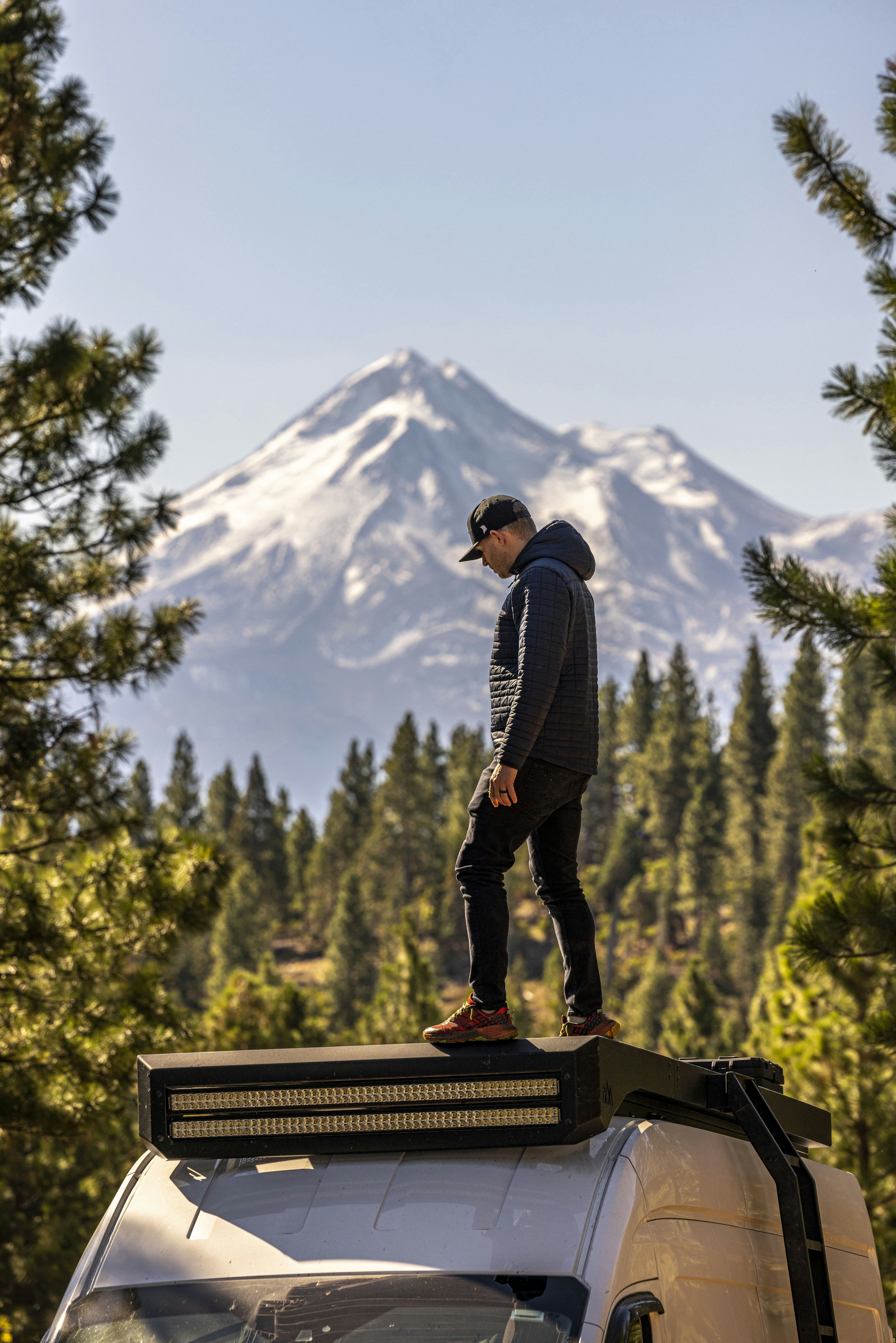 Un homme debout au sommet d’une camionnette devant une montagne