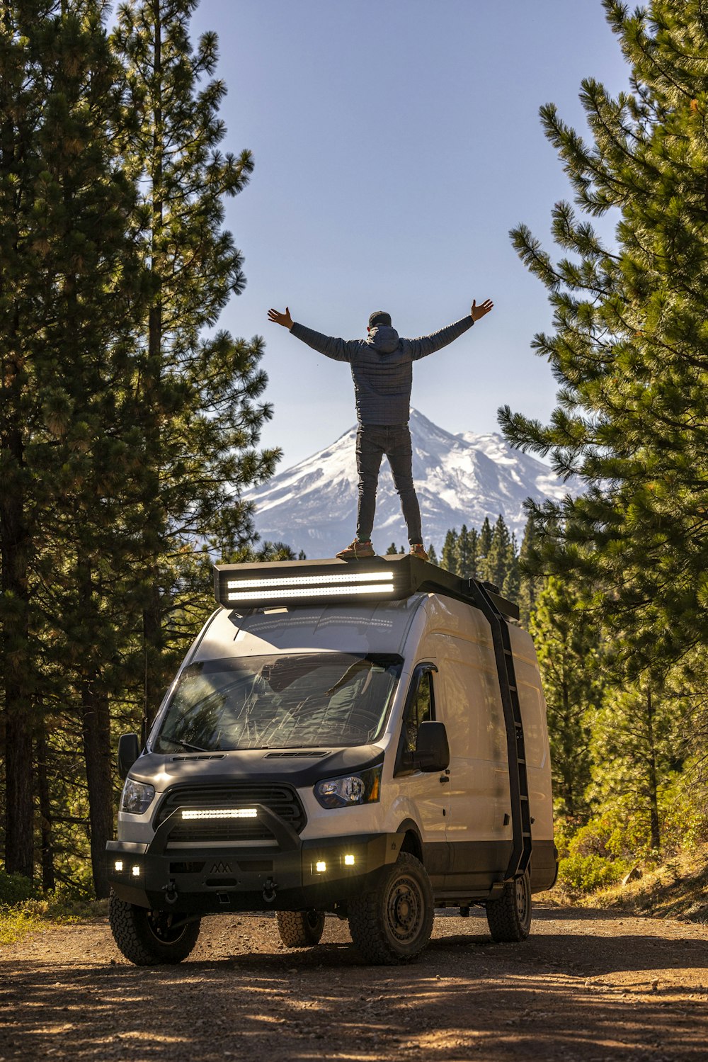 a man standing on top of a van in the woods