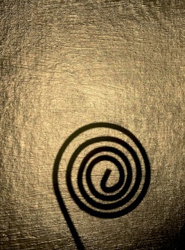 A spiral shadow cast on a textured, golden surface. The shadow is dark and well-defined against the shimmering background, creating an interesting visual contrast.