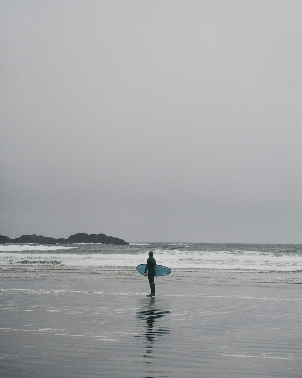 젖은 해변에서 서핑 보드를 들고있는 사람
