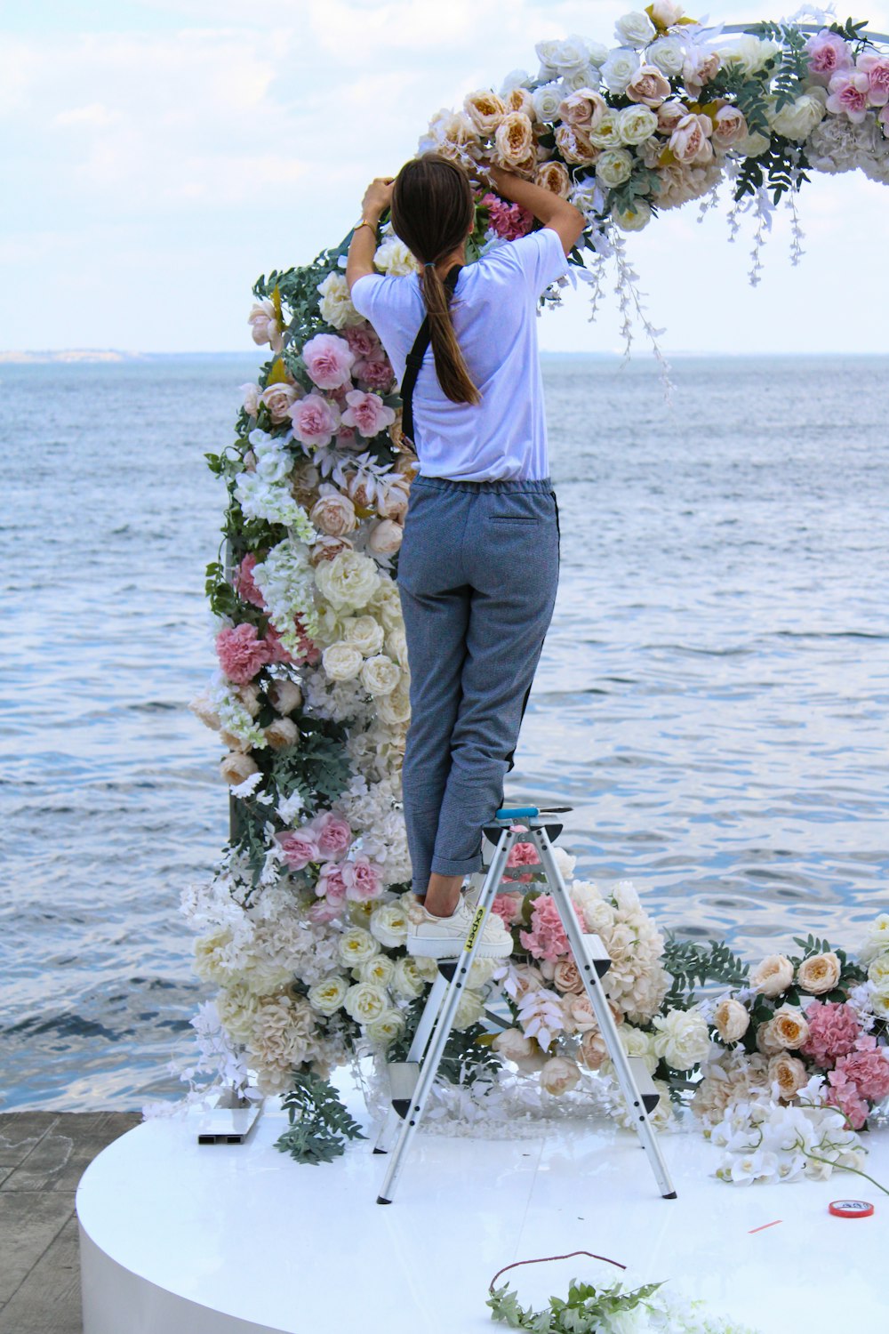 a woman standing on a ladder next to a flower arch