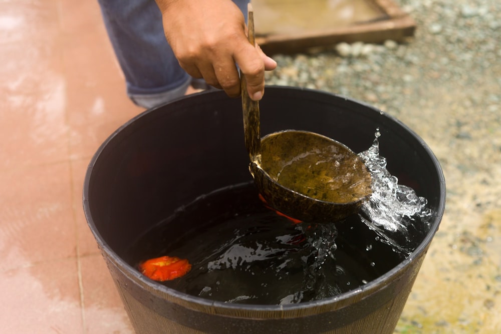 a person holding a wooden spoon in a bucket filled with water