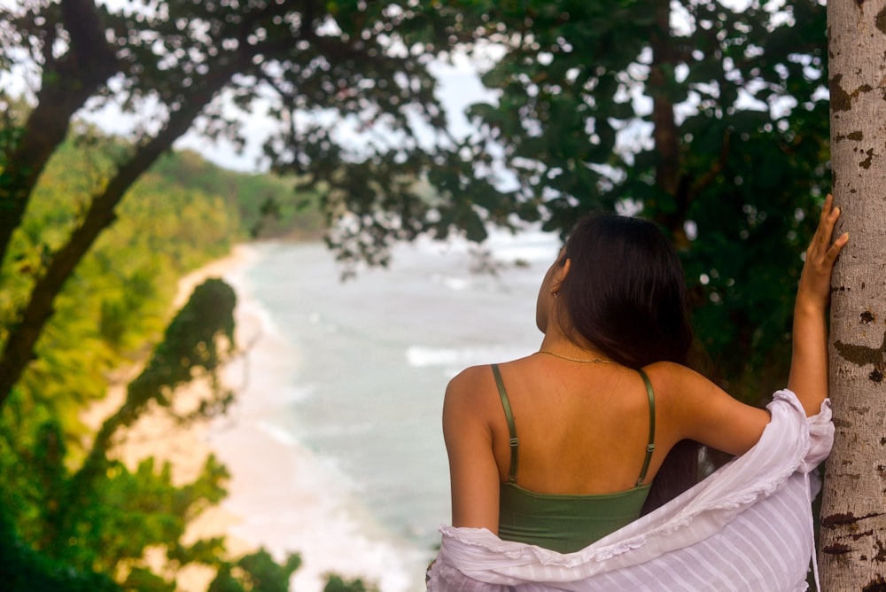 a woman standing next to a tree looking at the ocean