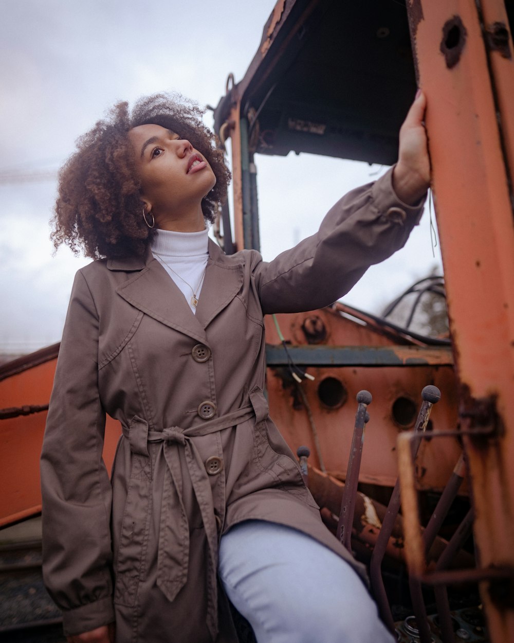 a woman in a trench coat leaning against a rusted truck